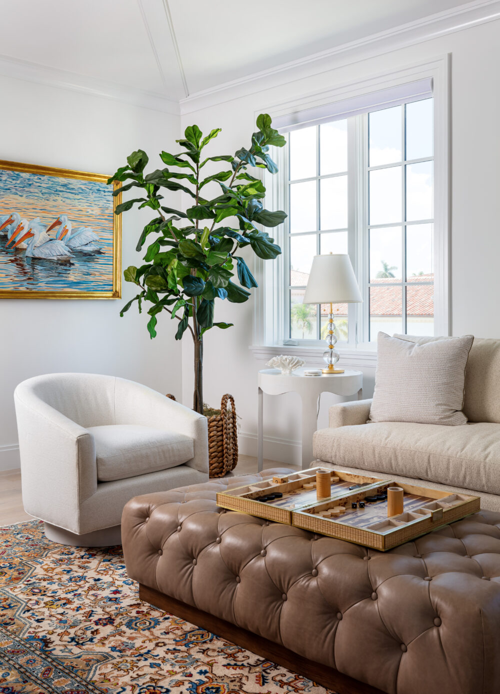 corner of living room with potted tree, white chair, and tufted leather ottoman
