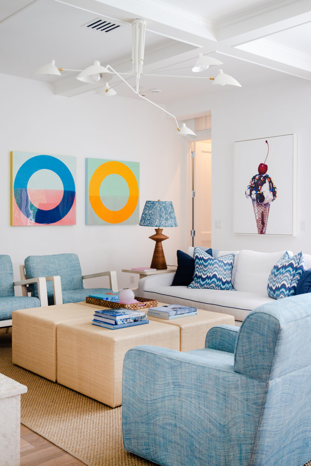 living room with colorful wall art, white sofa, blue chairs and pillows, and tan coffee table