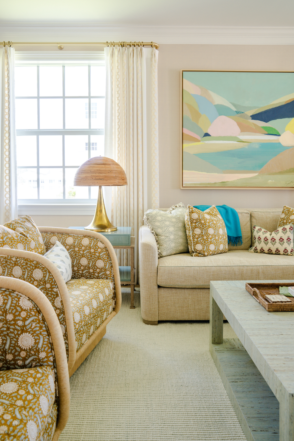 corner of living room with beige sofa and chairs, multicolor wall art, and rounded table lamp next to window