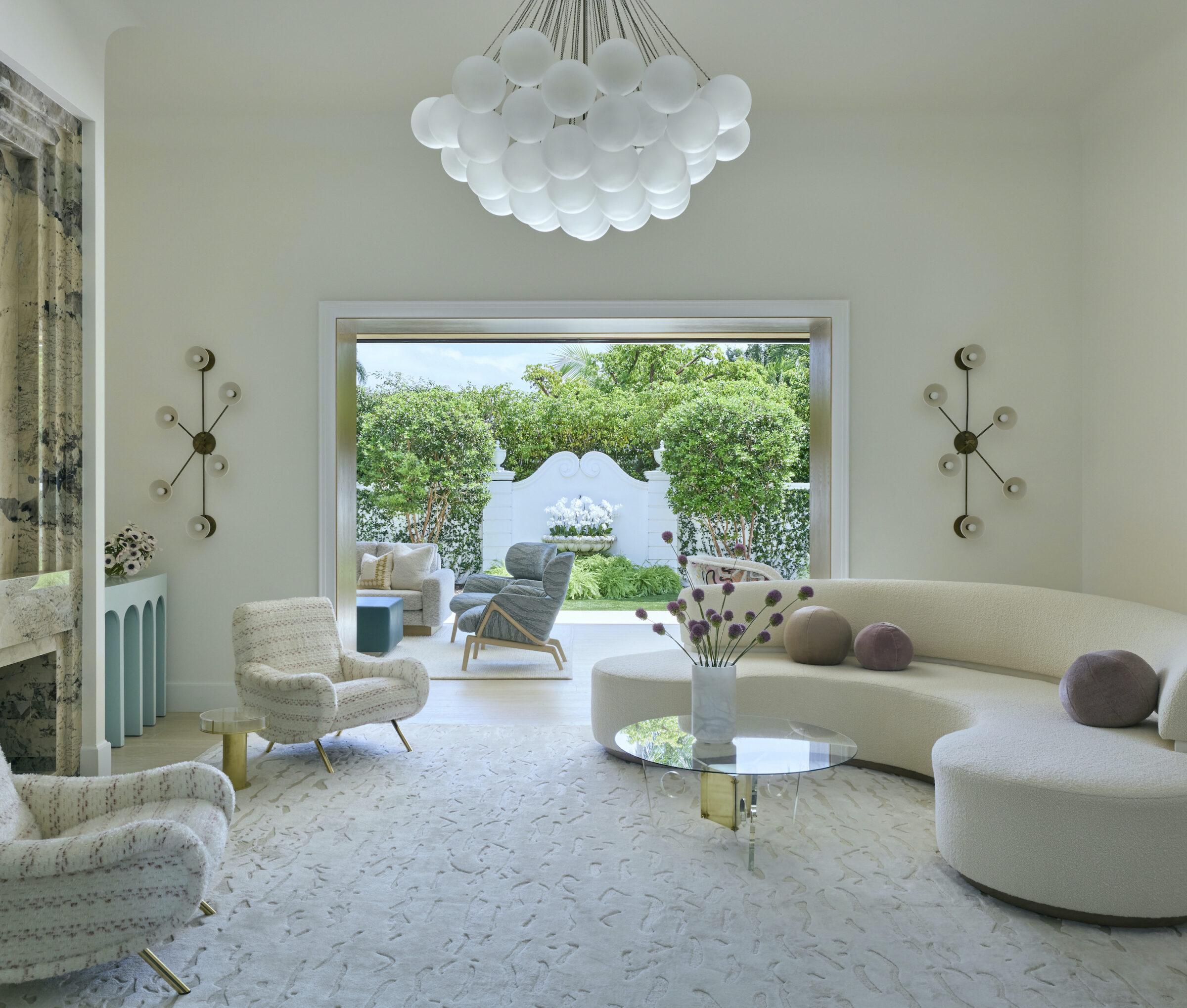 modern living room with rounded sofa, two chairs and doors opened to a tropical backyard