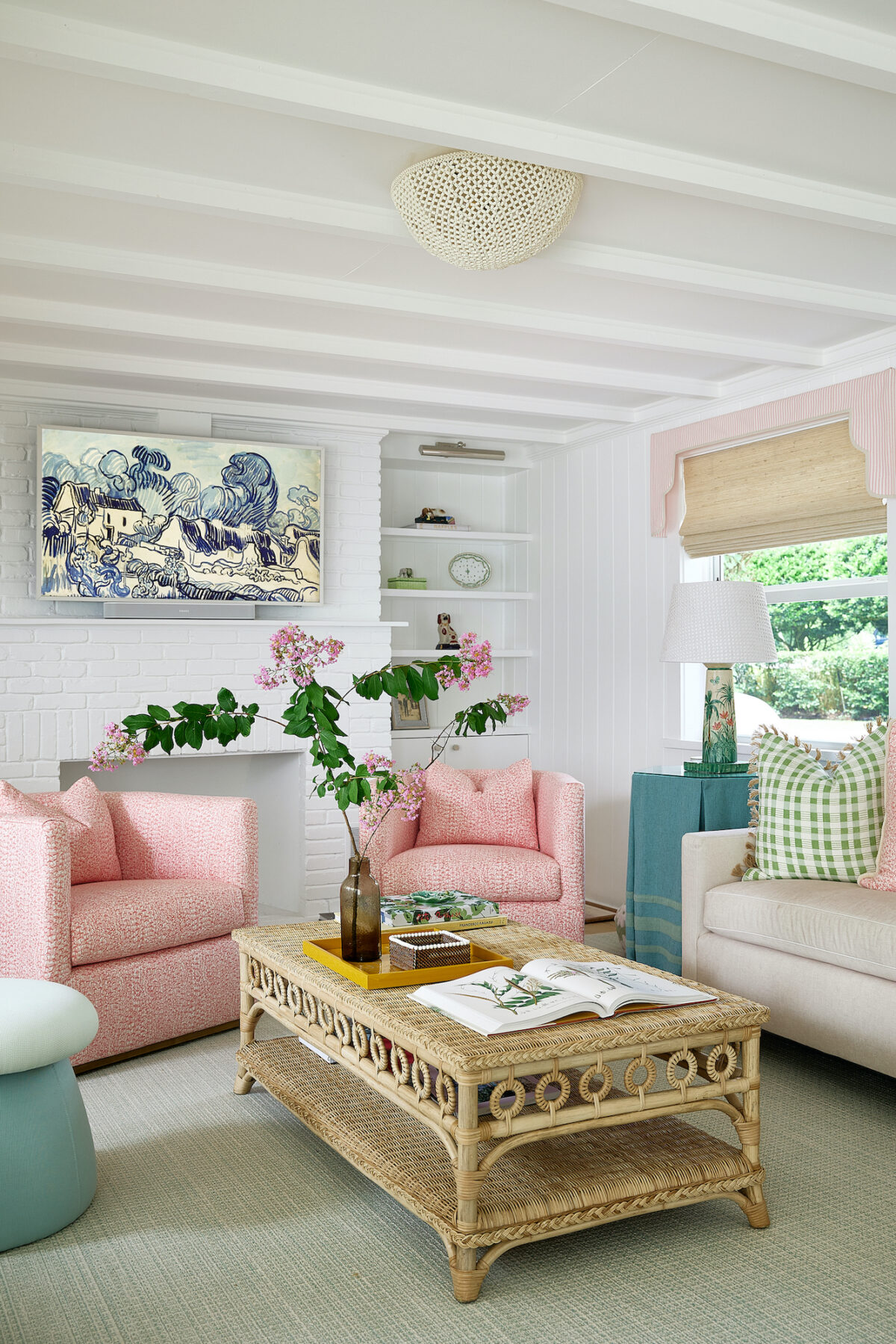 sitting area with white fireplace, 2 pink chairs, a rattan coffee table, and painted lamp next to a window